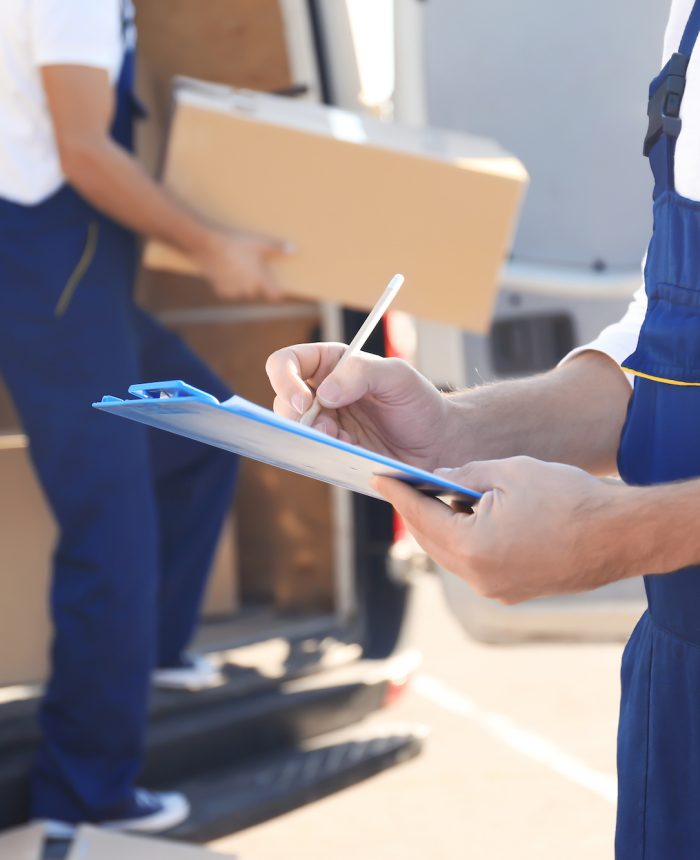 Delivery man checking list on clipboard near car